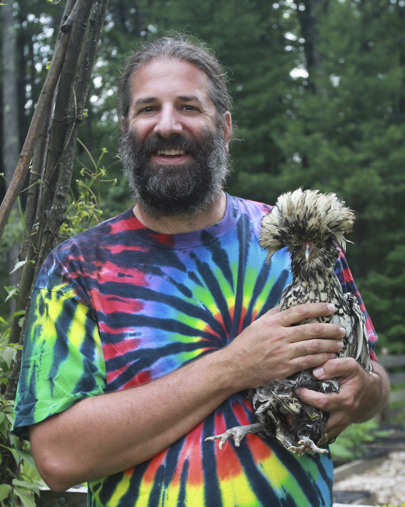 "A smiling Eric Simon holding a very flamboyant backyard chicken"