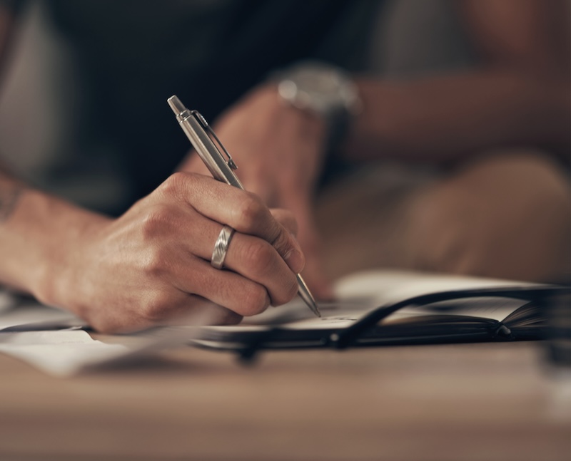 A male watch-clad hand and arm writing on a pad of paper