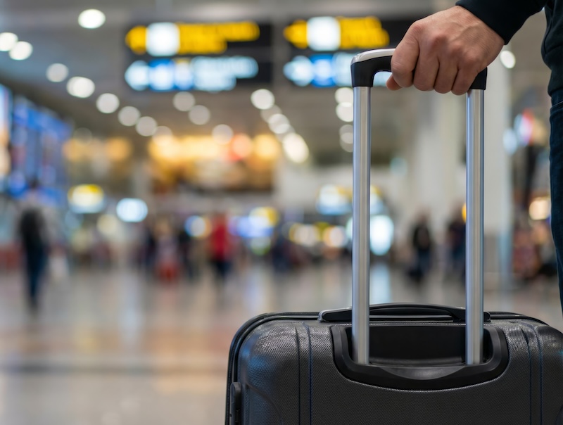 A hand wheeling a suitcase through an airport
